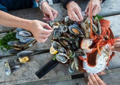 several hands reaching towards a seafood platter containing green-lipped mussels and crayfish