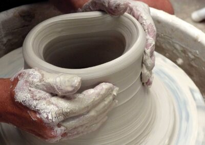 two hands working on a rotating ceramic vessel on a potters wheel