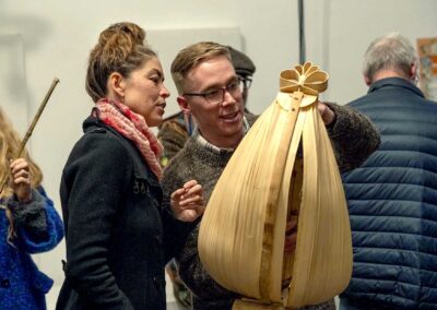 a woman and a man examining with curiosity a sand-coloured form made from natural fibre which is suspended from the ceiling