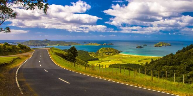 curved road trhough green grassy hills with blue sea in background and beautiful tufty white clouds on blue sky